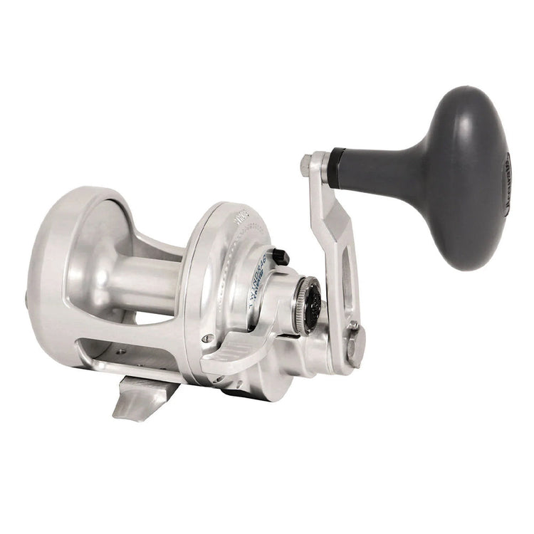 A shiny silver fishing reel with a large black handle, featuring a sturdy metal frame and intricate components for adjusting and controlling the line.