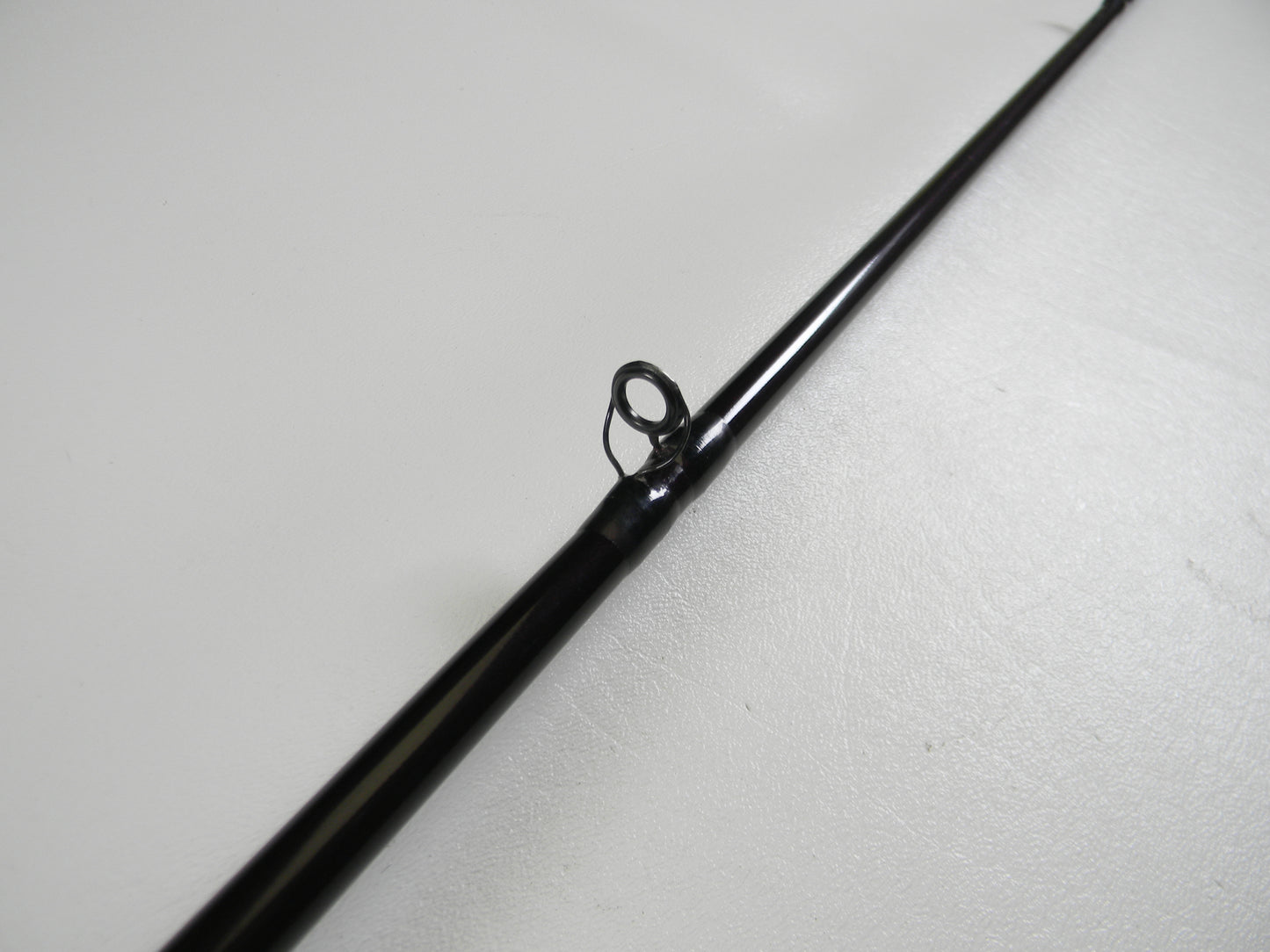 Close-up of a St. Croix Mojo Bass MJC68MF Jerkbait 6'8" Medium casting rod tip in black, featuring a single guide ring on a light surface, ideal for those seeking an upgrade through our trade-in program to earn store credit.
