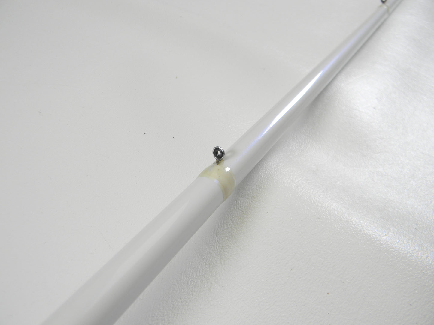 A used Duckett White Ice DFWI711HC Byron Velvick 7'11" Heavy A-Rig/Swimbait casting rod, in very good condition, resembles a fishing pole and features a small metal ball near one end. It rests diagonally on a smooth white surface, hinting at its past in angling adventures from the Rod and Reel Trade-In Program.