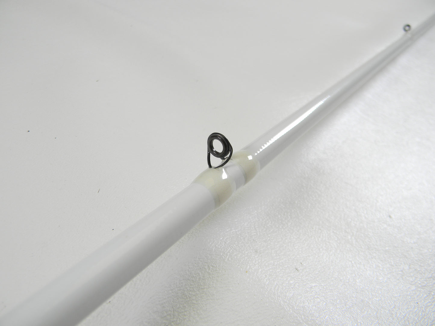 Close-up of a white Duckett Micro Magic Pro DFMP69MHC 6'9" Medium Heavy casting rod with a metal guide loop against a white background, highlighting its sleek design. Ideal for those participating in our Rod and Reel Trade-In Program to earn store credit or upgrade used gear.