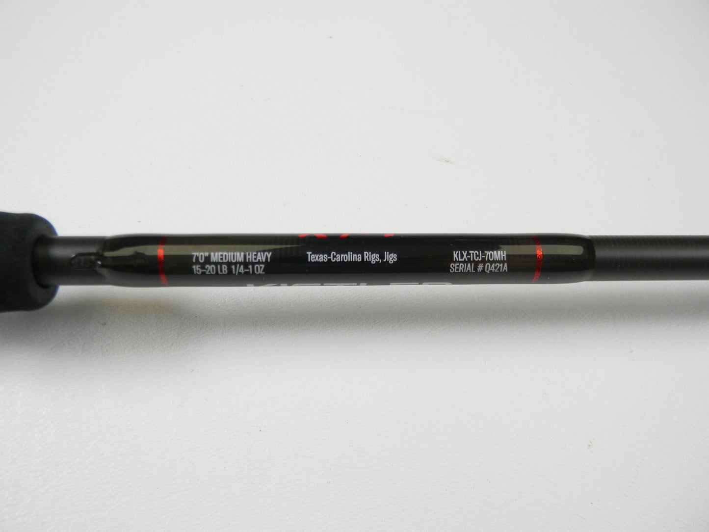 Close-up of a Lew's Kistler KLX KLX-TCJ-70MH casting rod in excellent condition shows "7'0” Medium Heavy," supports "15-20 lb" and "1/4-1 oz," good for Texas-Carolina Rigs and Jigs. Visible model number is “KLX-TC3-70MH” with serial "#04214." Ideal for trading up through our Rod and Reel Trade-In Program.
