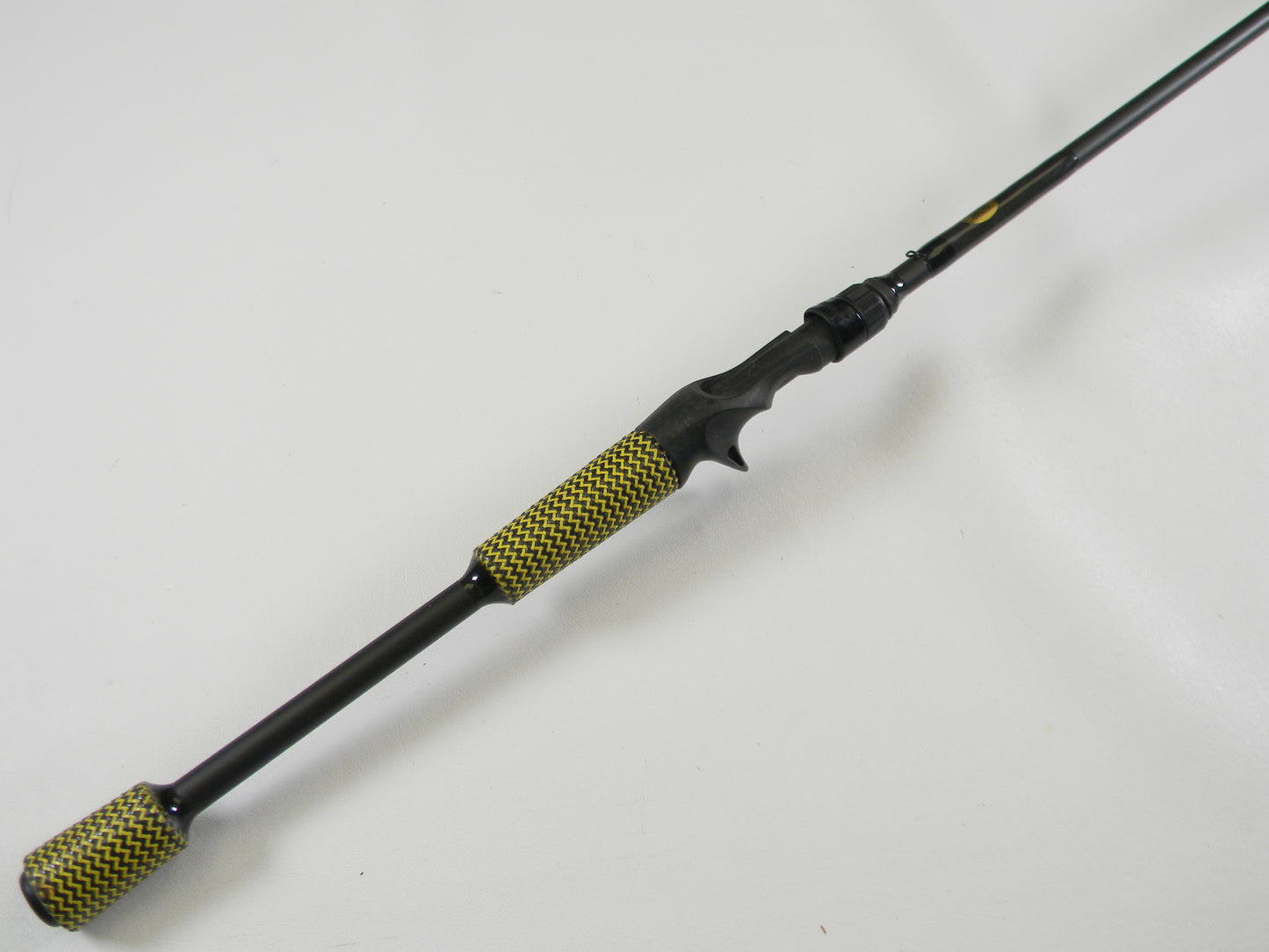 The used Cashion F90474b 7'4" Medium Heavy Casting Rod in very good condition lies on a white surface, featuring a black design with a yellow and black pattern on the handle and butt end, perfect for your next fishing adventure or to trade in for store credit.