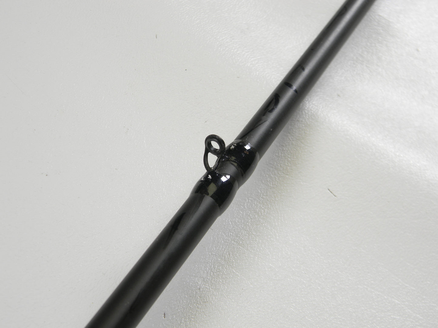 A close-up of a Cashion F90474b 7'4" Medium Heavy used casting rod in very good condition, lying on a white surface, highlights a black line guide loop. This fishing rod may qualify for our Rod and Reel Trade-In Program.