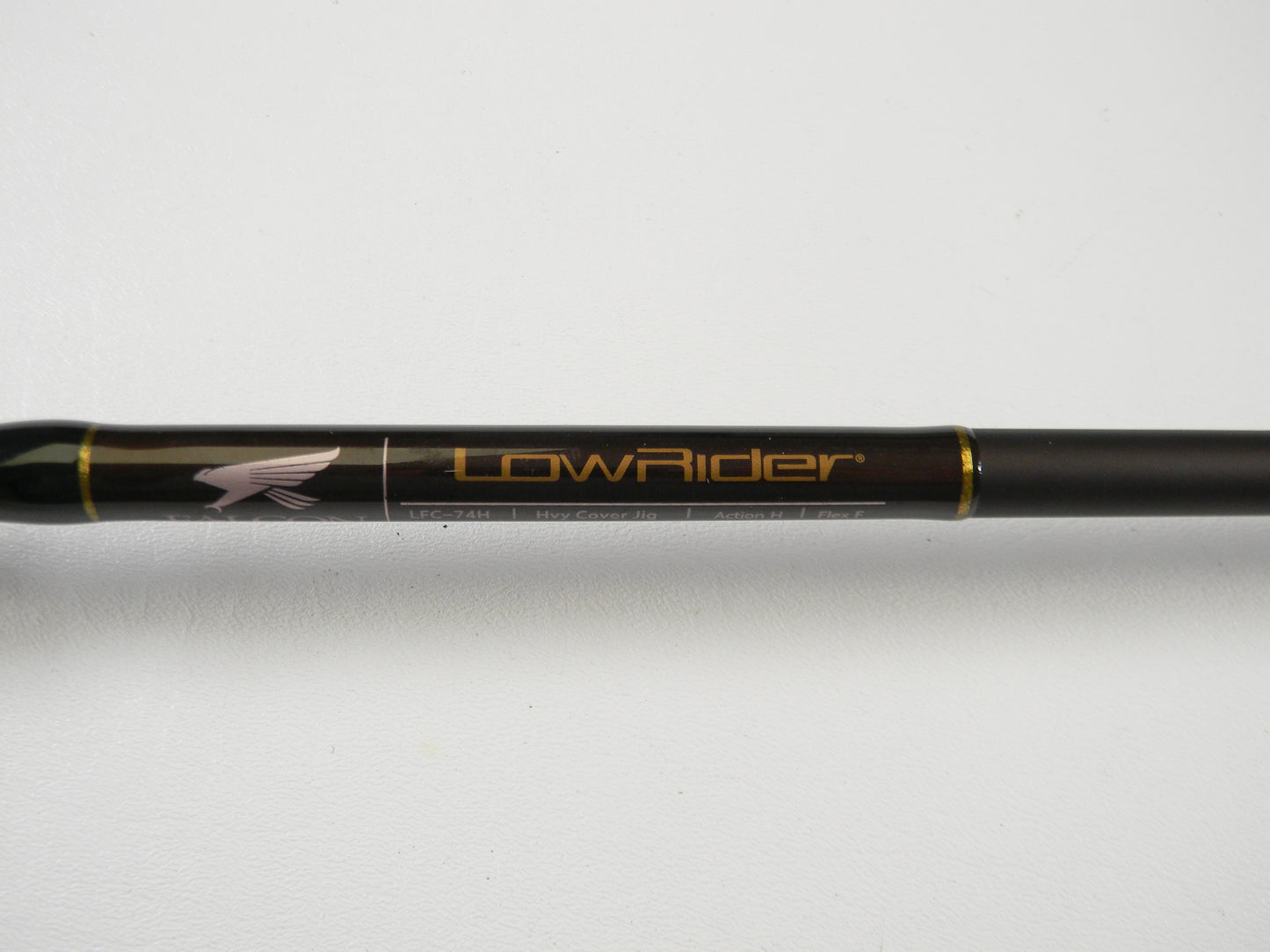 Close-up of a Falcon Lowrider LFC74H Heavy Cover Jig 7'4" fishing rod, featuring a bird in flight graphic and a sleek dark finish with gold accents. Perfect for upgrading your gear through our Rod and Reel Trade-In Program.