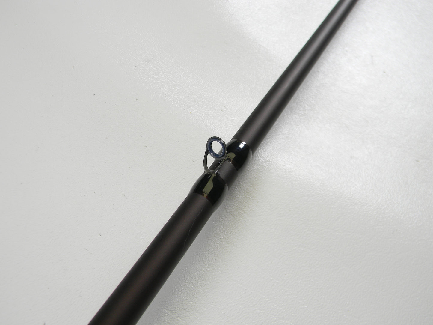 The photo showcases a Falcon Lowrider LFC74H Heavy Cover Jig 7'4" Heavy casting rod in excellent condition. Its black guide loop with a metallic ring stands out against the light background. Ideal for those participating in our Rod and Reel Trade-In Program to upgrade their gear.