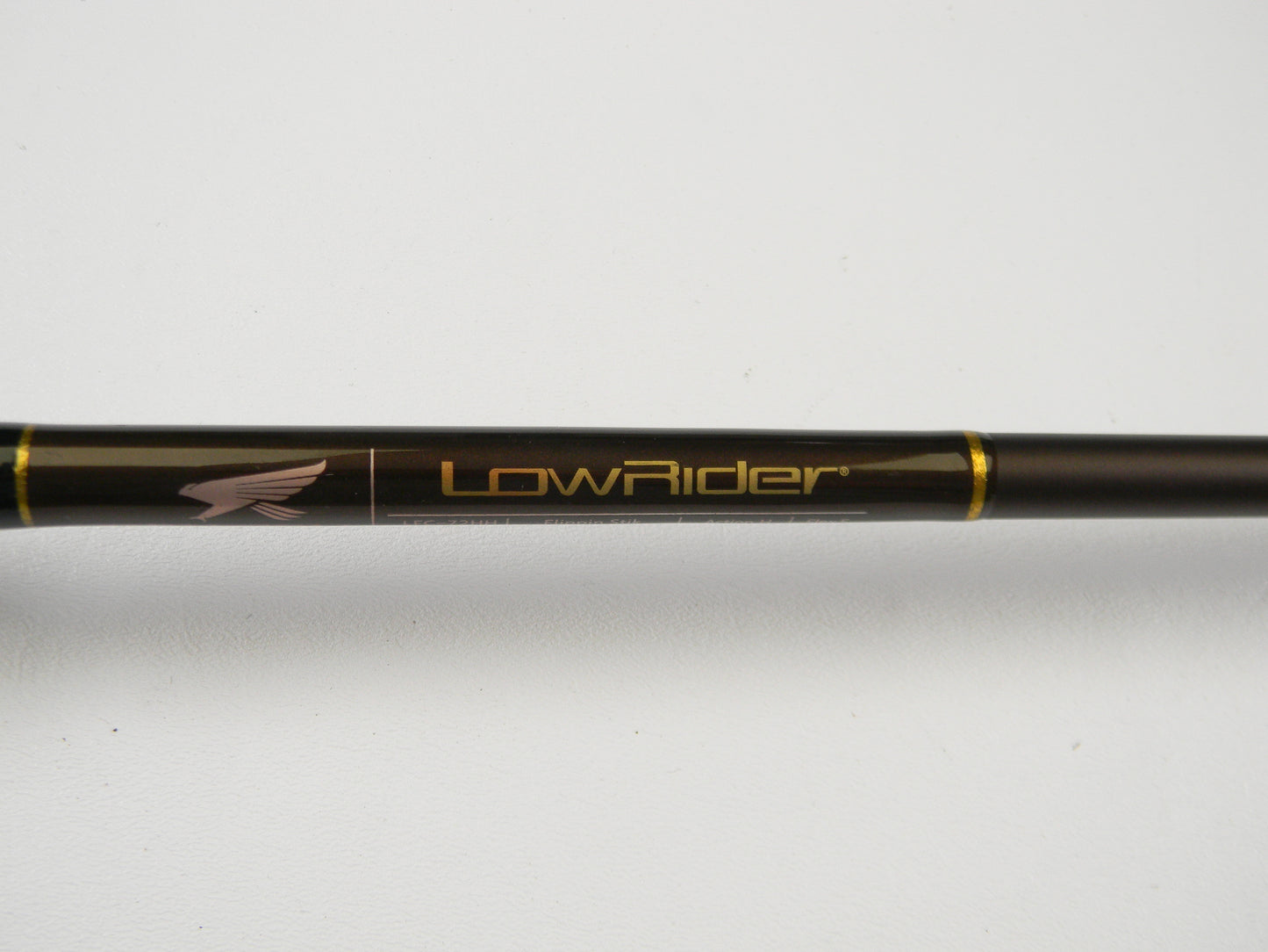 Close-up of the Falcon Lowrider LFC-72HH Flippin Stik 7'2" Heavy in black with gold accents, featuring "LowRider" and an eagle logo. Perfect for trade-in programs, this rod offers anglers store credit on used gear. Set against a plain white surface, it highlights its sleek design.