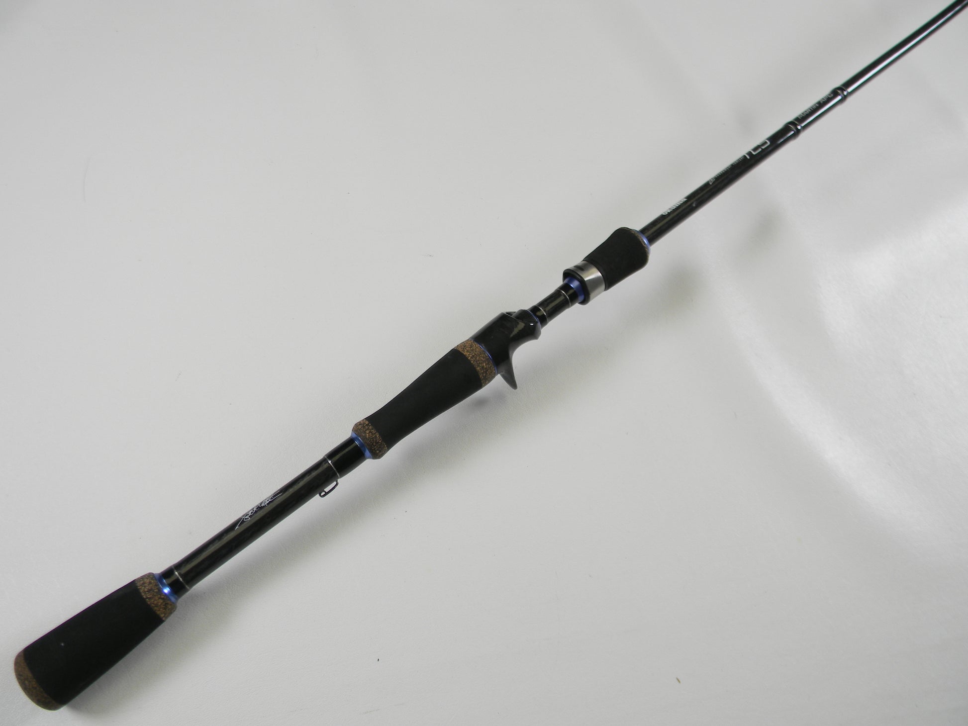 The Okuma TCS TCS-C-701MH 7'0" Medium Heavy rod, featuring a black design with a cork handle and blue accents, is displayed on a white surface. Its sleek build offers comfort and style, ideal for upgrading in our Rod and Reel Trade-In Program if you have used gear.