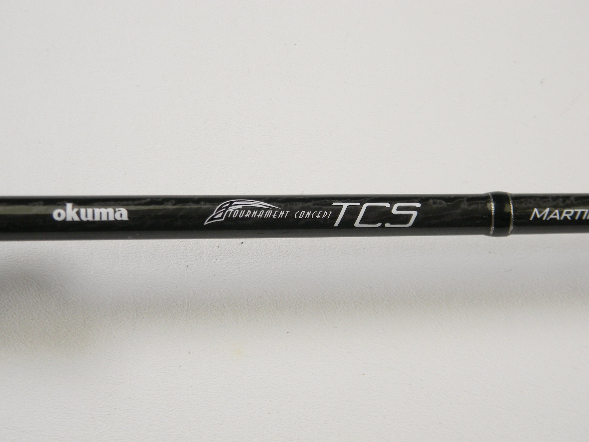 Close-up of a black fishing rod with "Okuma TCS TCS-C-701MH 7'0" Medium Heavy" printed on it against a white background. Ideal for upgrading through our Rod and Reel Trade-In Program, offering store credit on used gear.