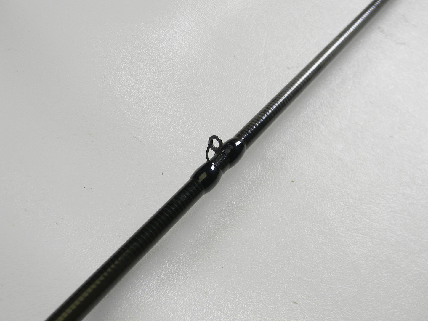 Check out the close-up of the Cashion Icon Series iBFS610MLF 6'10" Medium Light - Used Casting Rod, featuring a metal guide loop, part of our used gear selection. This dark-colored rod rests on a light surface and is perfect for those utilizing our Rod and Reel Trade-In program for store credit.