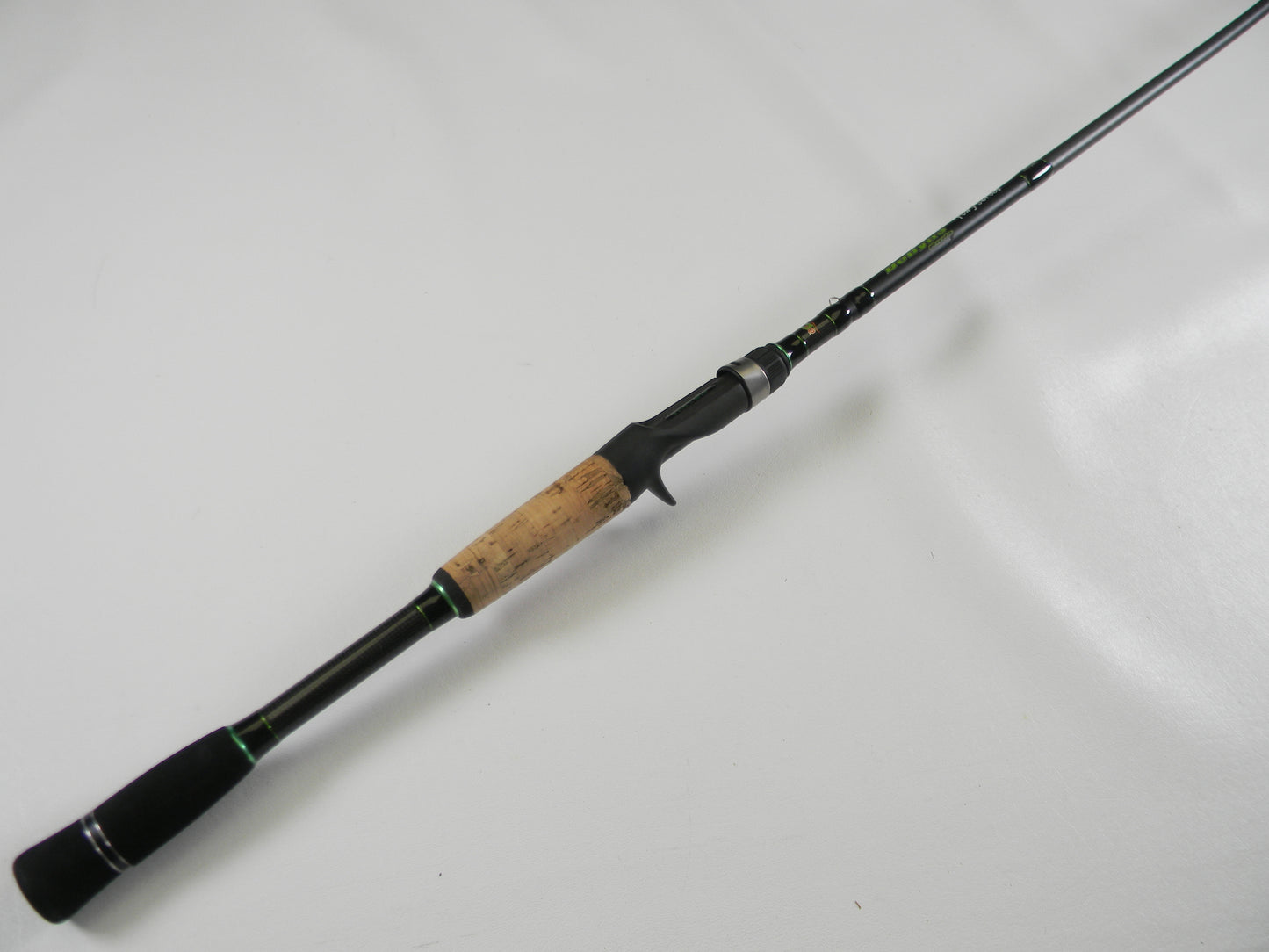 The Dobyns Fury FR734C, a sleek 7'3" black and green fishing rod with a cork grip handle, lies diagonally on a white surface. This lightweight used casting rod is in excellent condition and part of our Rod and Reel Trade-In Program, perfect for optimal casting.