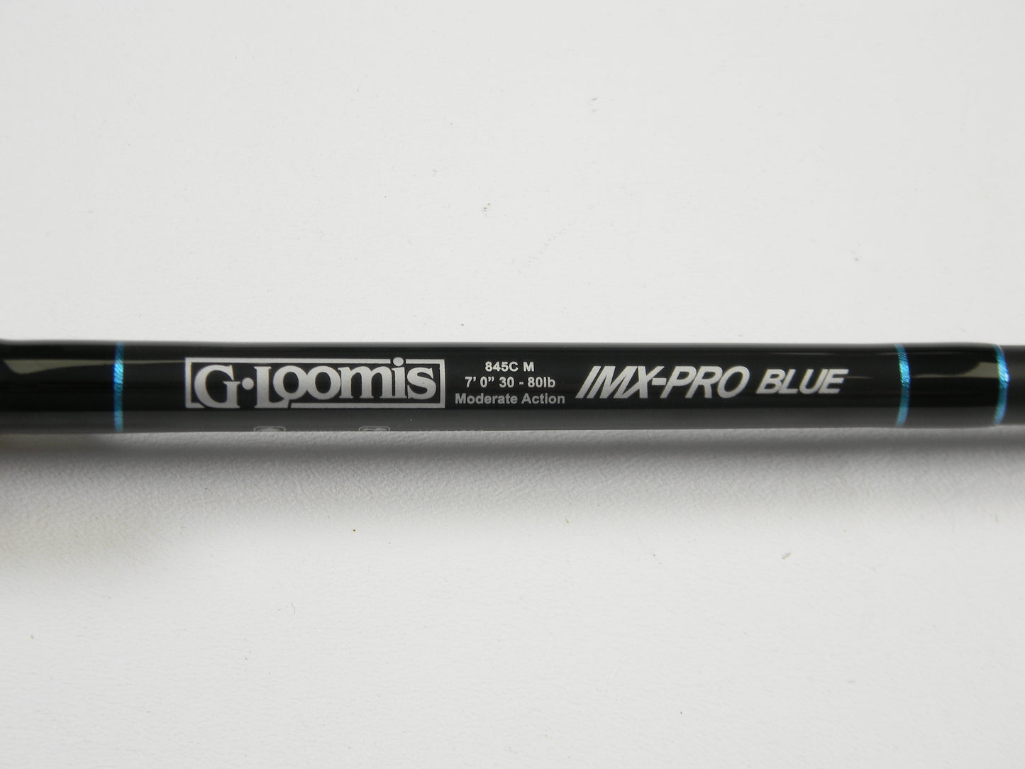 A close-up of a used G. Loomis IMX-PRO Blue 845C M 7'0" Heavy Casting Rod in excellent condition, shown on a white background with blue accents. Ideal for those interested in used gear or our Rod and Reel Trade-In Program.