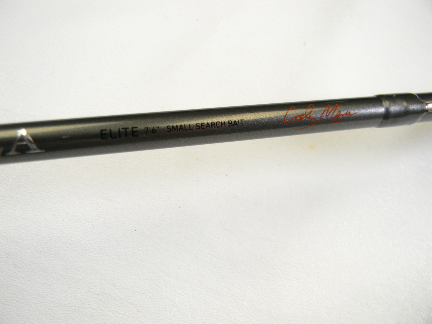 Close-up of a Daiwa Tatula Elite TTEL761MHRB 7'6" Medium Heavy Casting Rod, ideal for the Rod and Reel Trade-In Program. The dark rod, in mint condition, features a red signature against a plain white background.