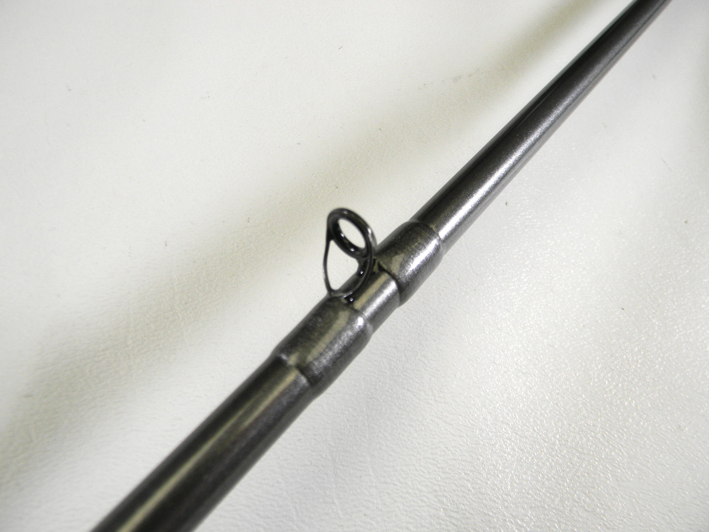 A close-up of a guide on a sleek Daiwa Tatula Elite TTEL761MHRB rod against a white background highlights its smooth and metallic finish, ideal for those looking to upgrade through our Rod and Reel Trade-In Program.
