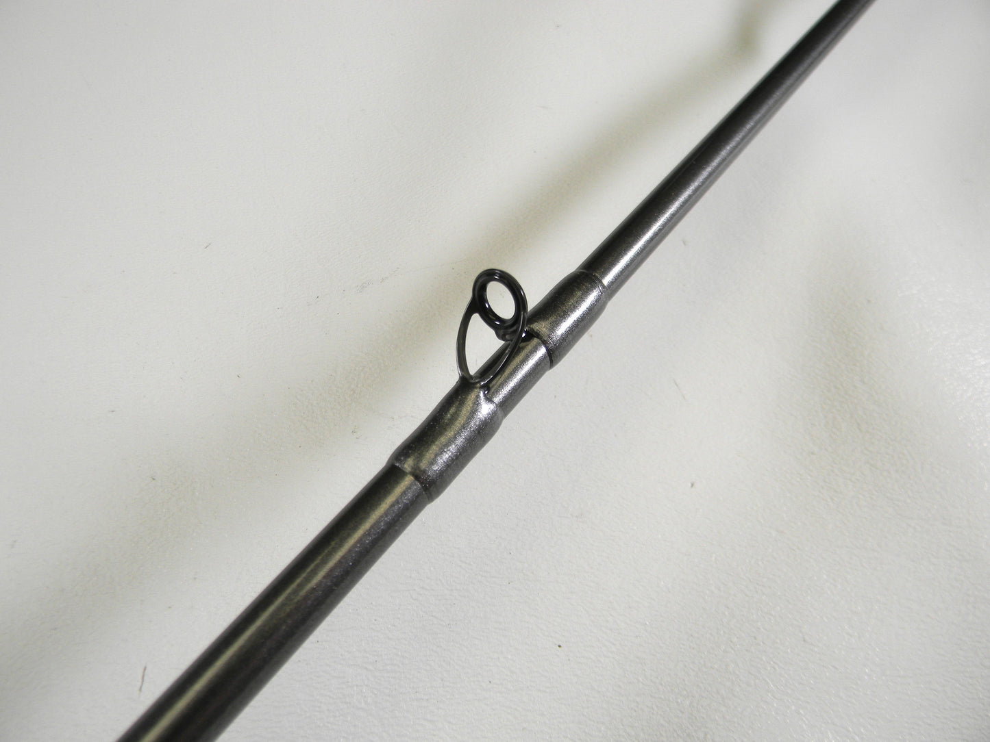 Close-up of a Daiwa Tatula Elite TTEL751MHFB, highlighting its metal guide ring on a dark pole against a light background. Perfect for our Rod and Reel Trade-In Program participants seeking quality gear, this 7'5" medium-heavy used rod is in mint condition.