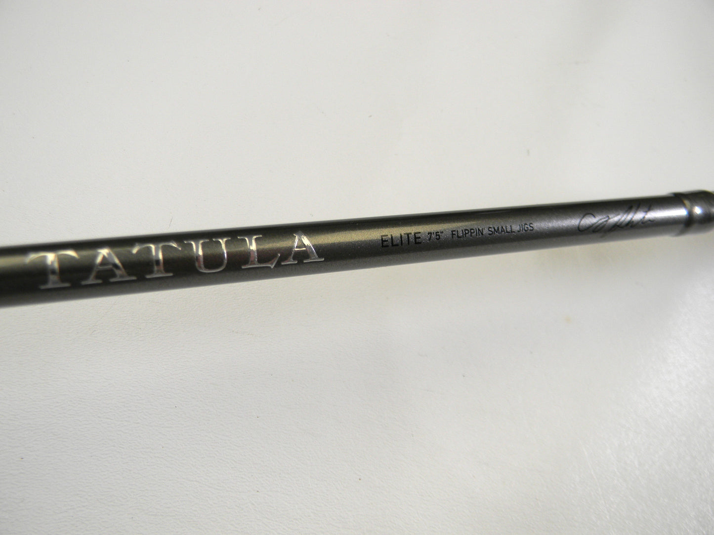 Close-up of a Daiwa rod displaying "Tatula" in large letters. Additional text reads "ELITE 7'5'' FLIPPIN' SHAUN KGS" against a plain white background. Explore our Trade-In program for store credit to upgrade your used gear.