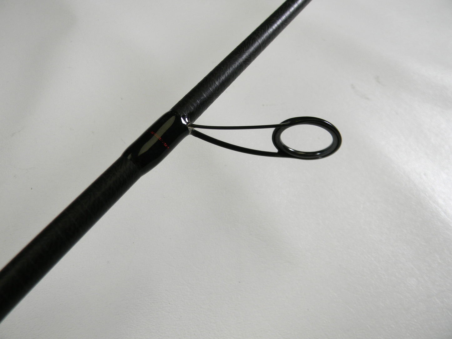 Close-up of the Ark Invoker Pro IVP71MXS 7'1" Medium - Used Spinning Rod in excellent condition, showcasing its textured finish and shiny metal guiding ring on a smooth white surface, embodying Ark Fishing's commitment to quality through our Rod and Reel Trade-In Program.