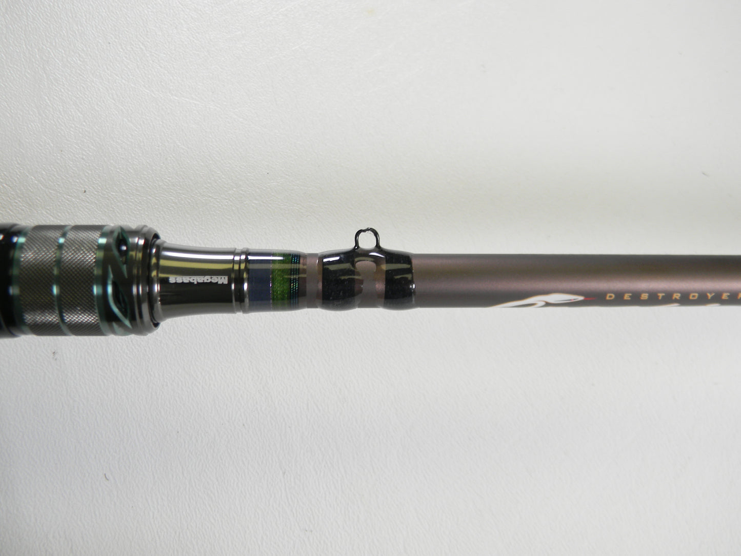 Close-up of a Megabass Orochi X10 F4-68XT Jabberwock 6'8" Medium Light casting rod handle and first line guide against white. The dark, metallic green-accented blank is ideal for our Rod and Reel Trade-In Program if upgrading used gear.