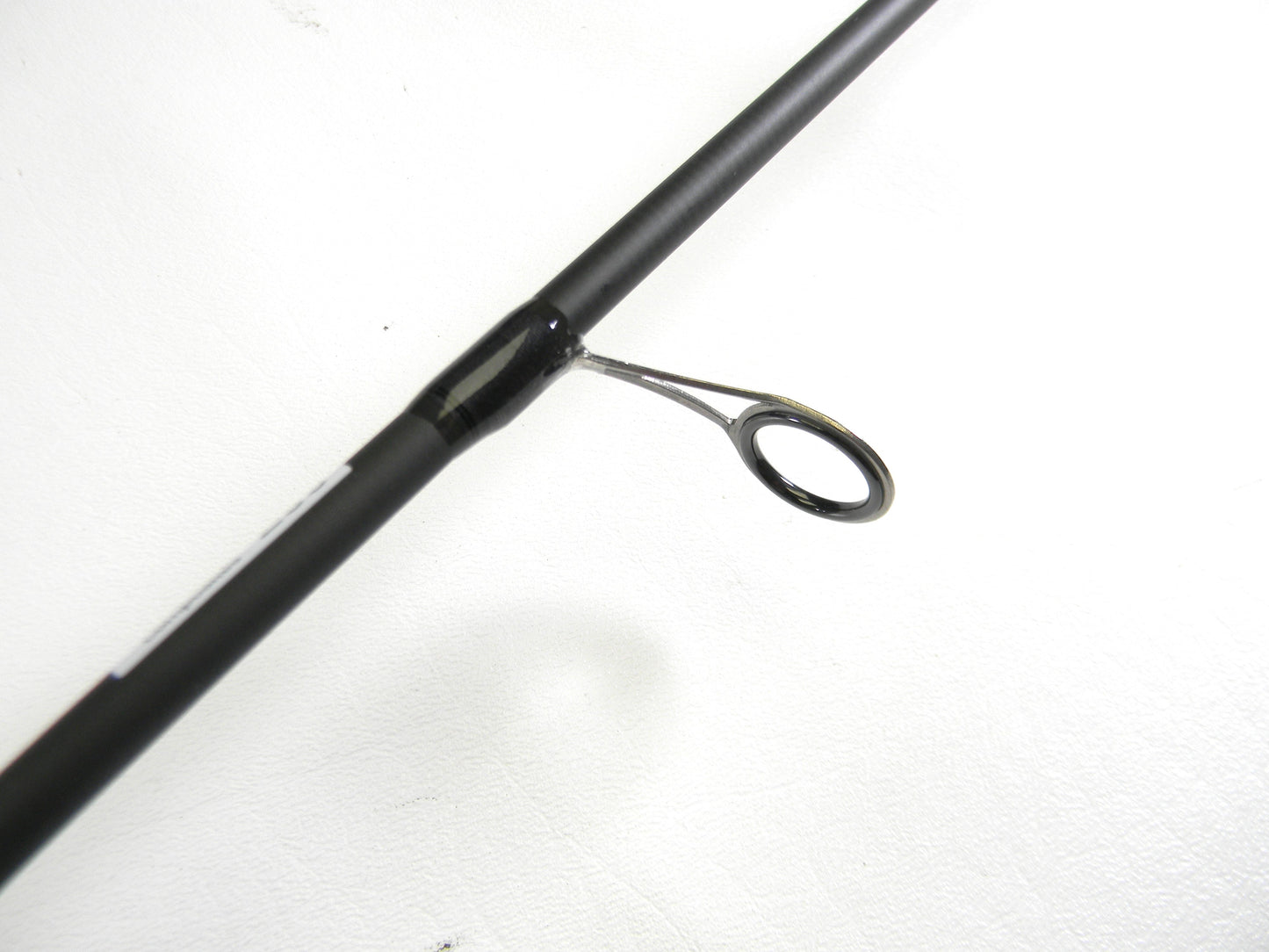 A close-up of an Abu Garcia Veritas Tournament VXTS610-4 6'10" Medium Light spinning rod guide against a white background is available through our Rod and Reel Trade-In program. The rod's black finish contrasts strikingly with the silver circular guide ring.