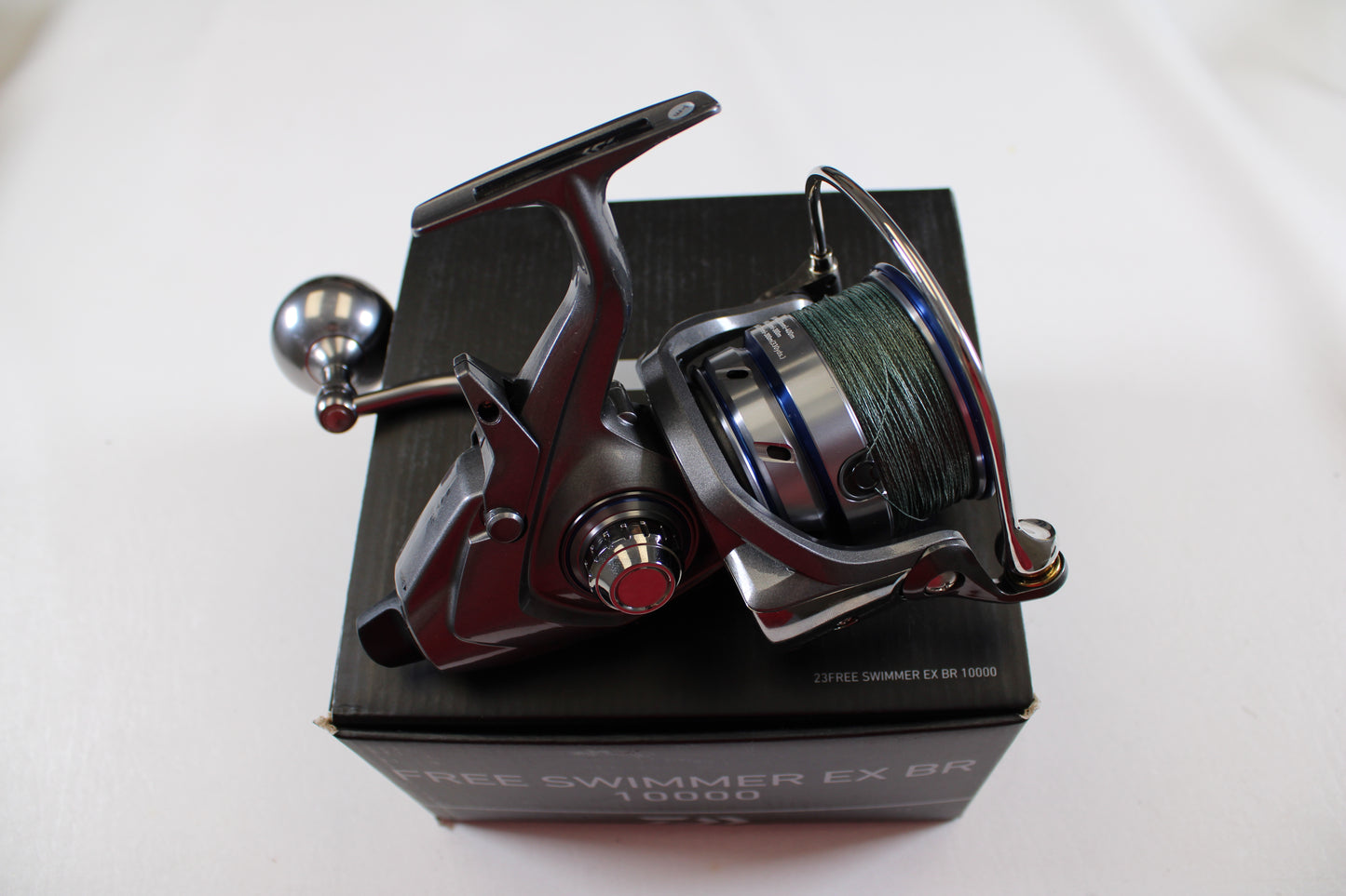 A Daiwa Free Swimmer EX BR 10000 used spinning reel in excellent condition, with a green fishing line spool, is mounted on a black box labeled "FREE SWIMMER EX BR 10000" against a plain white background—ideal for trade-in.