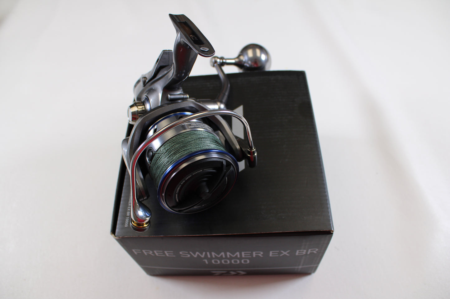 A used Daiwa Free Swimmer EX BR 10000 spinning reel with green line sits atop a black box, ideal for rod and reel trade-in programs; branded by Daiwa and set against a plain white background.