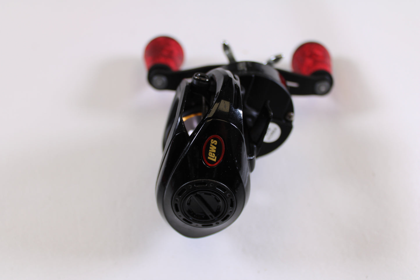 A close-up of a Lew's Tournament MB LFS TS1SHMBL 7.5:1 LH used casting reel in good condition, featuring black and red handles on a white surface—ideal for those interested in used gear or our Rod and Reel Trade-In Program.