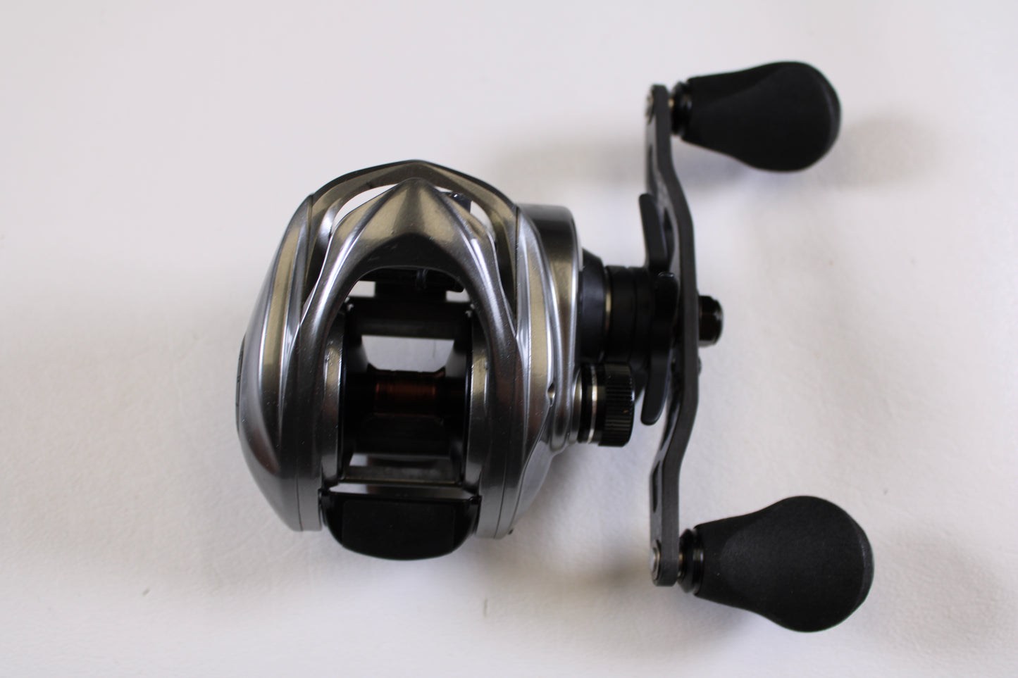 A Kistler Chromium 7.3:1 RH used casting reel in excellent condition, featuring a silver and black design with two black handles, is shown on a white surface.