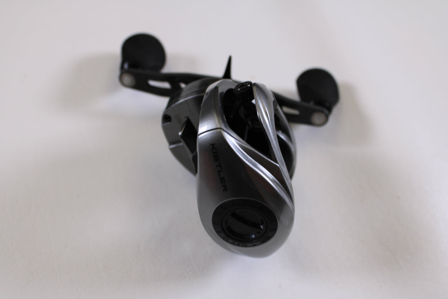 A close-up of a black Kistler Chromium 7.3:1 RH Used Casting Reel in excellent condition with dual handles on a white surface—ideal for our Rod and Reel Trade-In Program or quality used gear options.