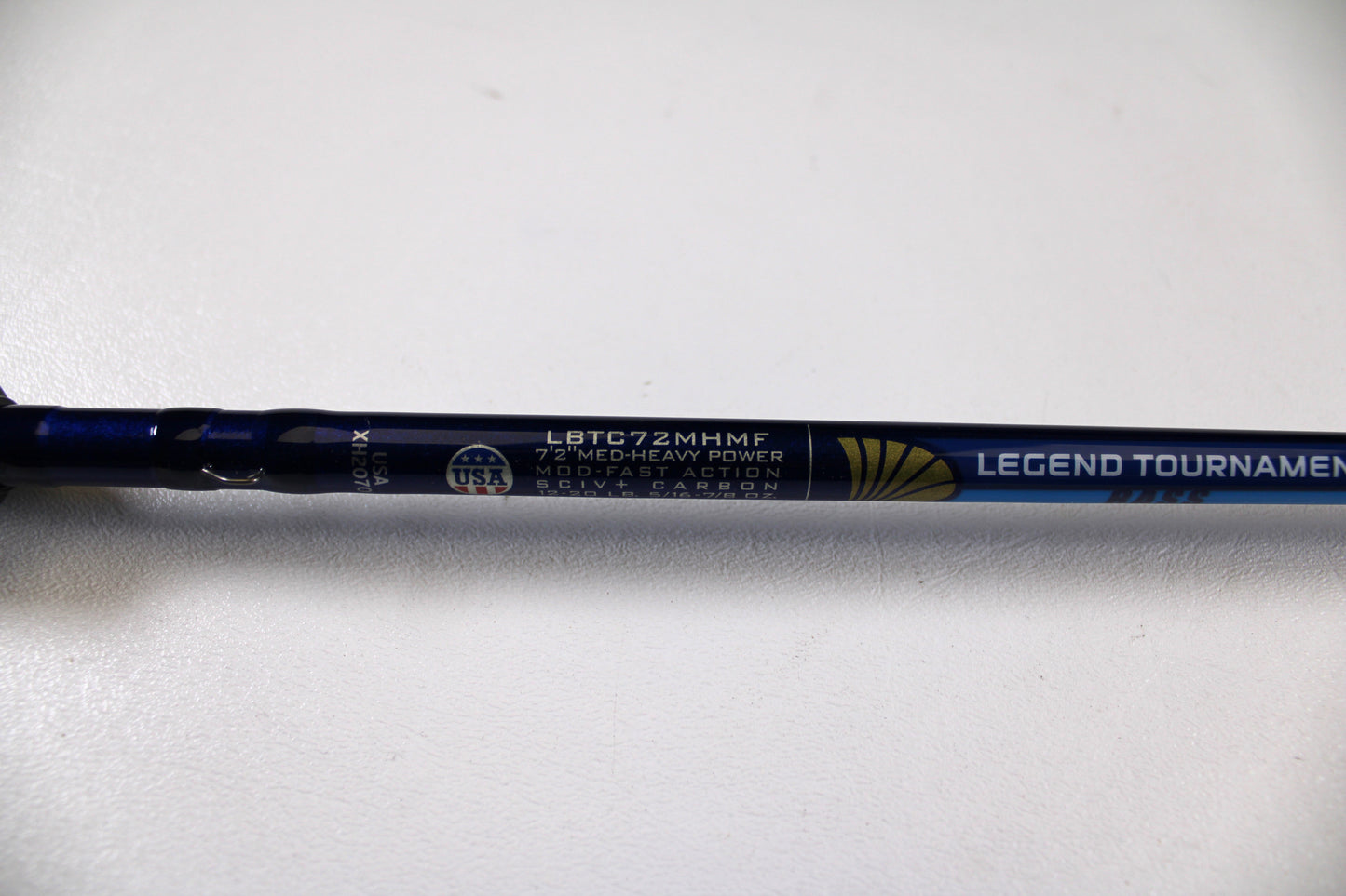 A close-up of a St. Croix Legend Tournament Bass LBTC72MHMF Finesse Carbon Cranker 7'2" Medium Heavy Used Casting Rod in excellent condition, with a USA flag emblem and Rod & Reel Trade-In Program details on metallic blue.
