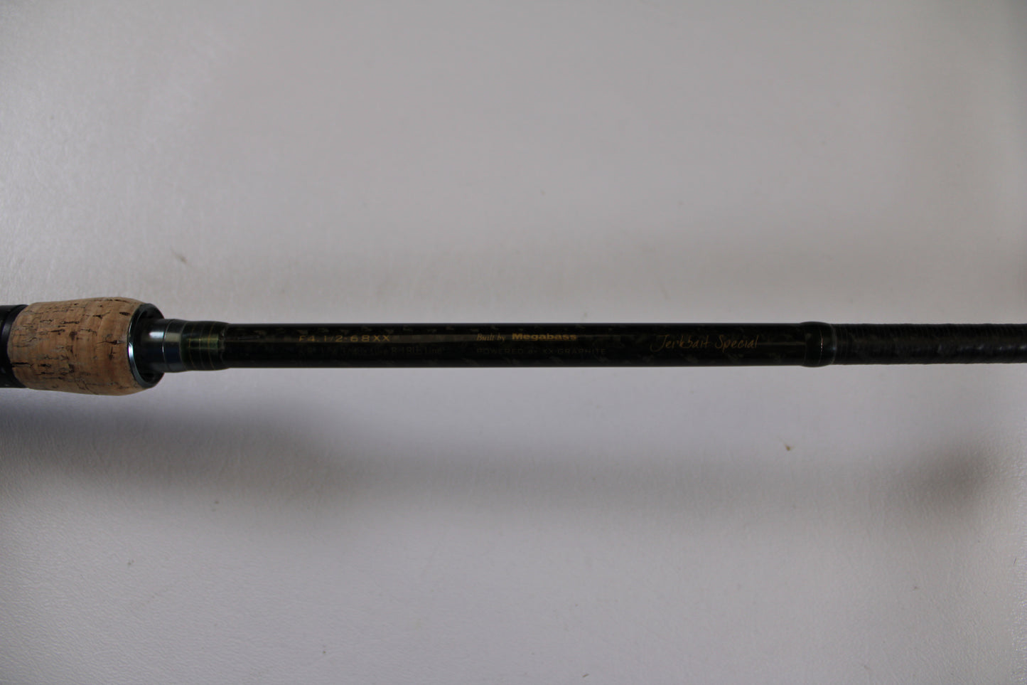 A close-up of the Megabass Orochi XX Aaron Martens F4.1/2-68XX Jerkbait Special casting rod handle (used, fair condition) with a cork grip and black shaft—ideal for trading in used gear during our Rod and Reel Trade-In event.