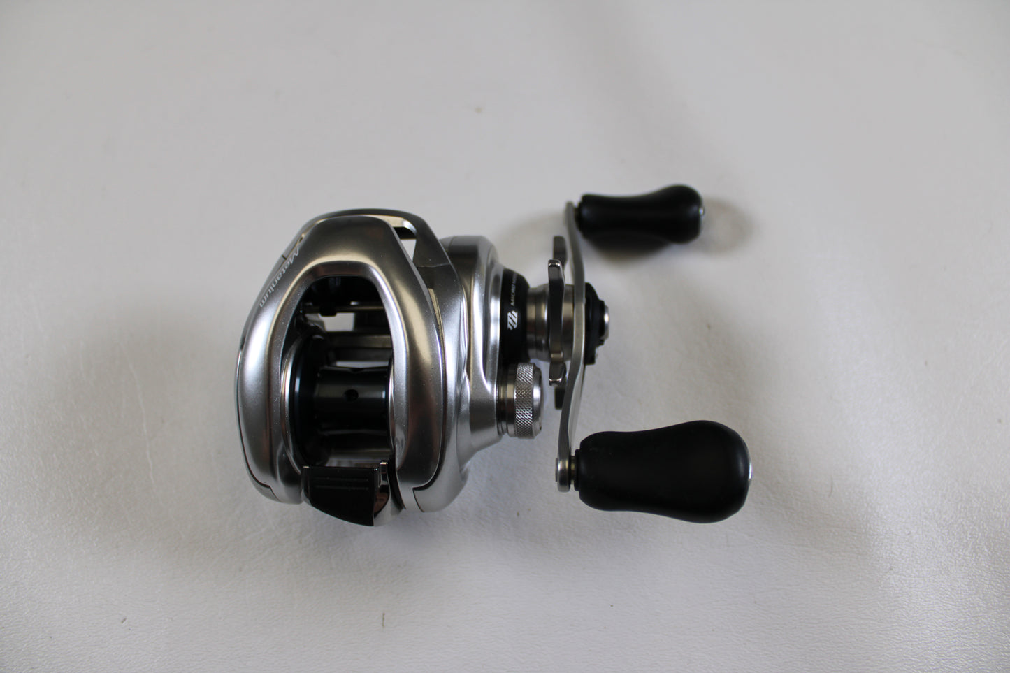 A Shimano Metanium MGL 150 6.2:1 used casting reel (very good condition) with two black handles is displayed on a plain white surface—ideal for upgrading or earning store credit through our Rod and Reel Trade-In Program.