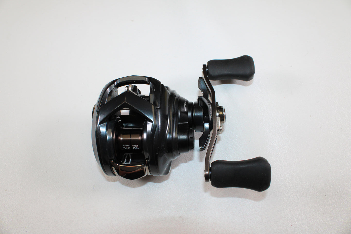 The Daiwa Tatula SV 70 TTUSV70XH Used Casting Reel—black with dual handles and a compact metallic design—is shown on a white background, ideal for trade-ins or store credit through our Rod and Reel Trade-In Program.