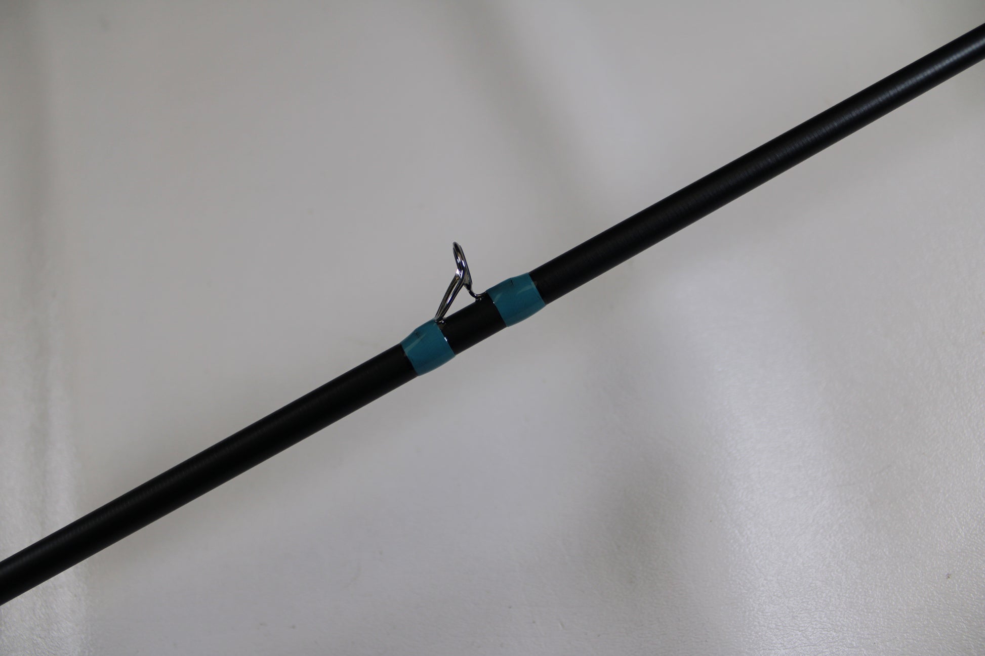 A close-up of the G. Loomis NRX+ 903C MBR Used Casting Rod in excellent condition, featuring a black blank, silver guide ring, and teal thread wrap—eligible for our Rod and Reel Trade-In Program to earn store credit for used gear.