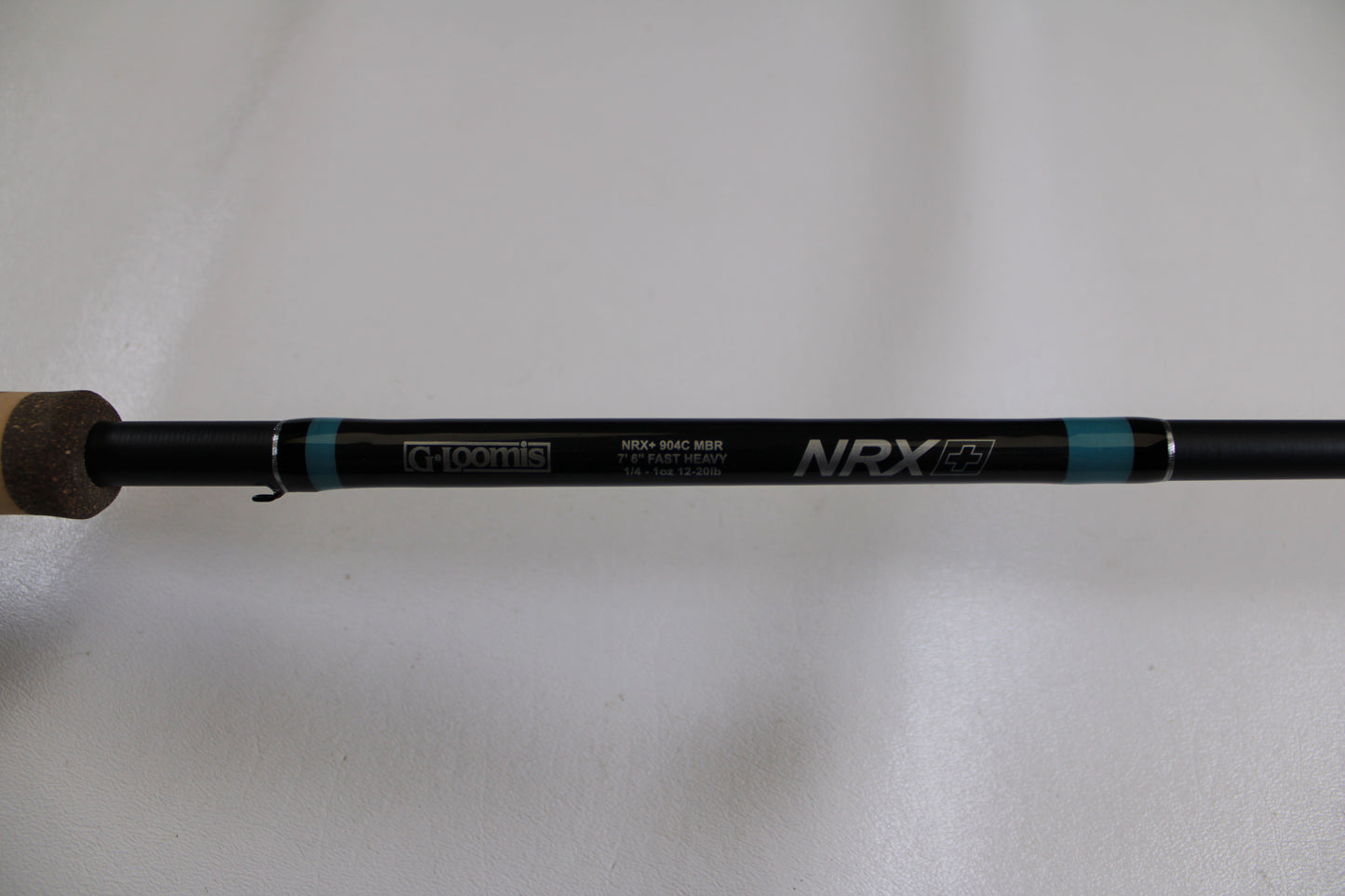 A close-up of a G. Loomis NRX+ 904C MBR Used Casting Rod in excellent condition, showing cork handle and brand logos on the black rod against a plain white background.