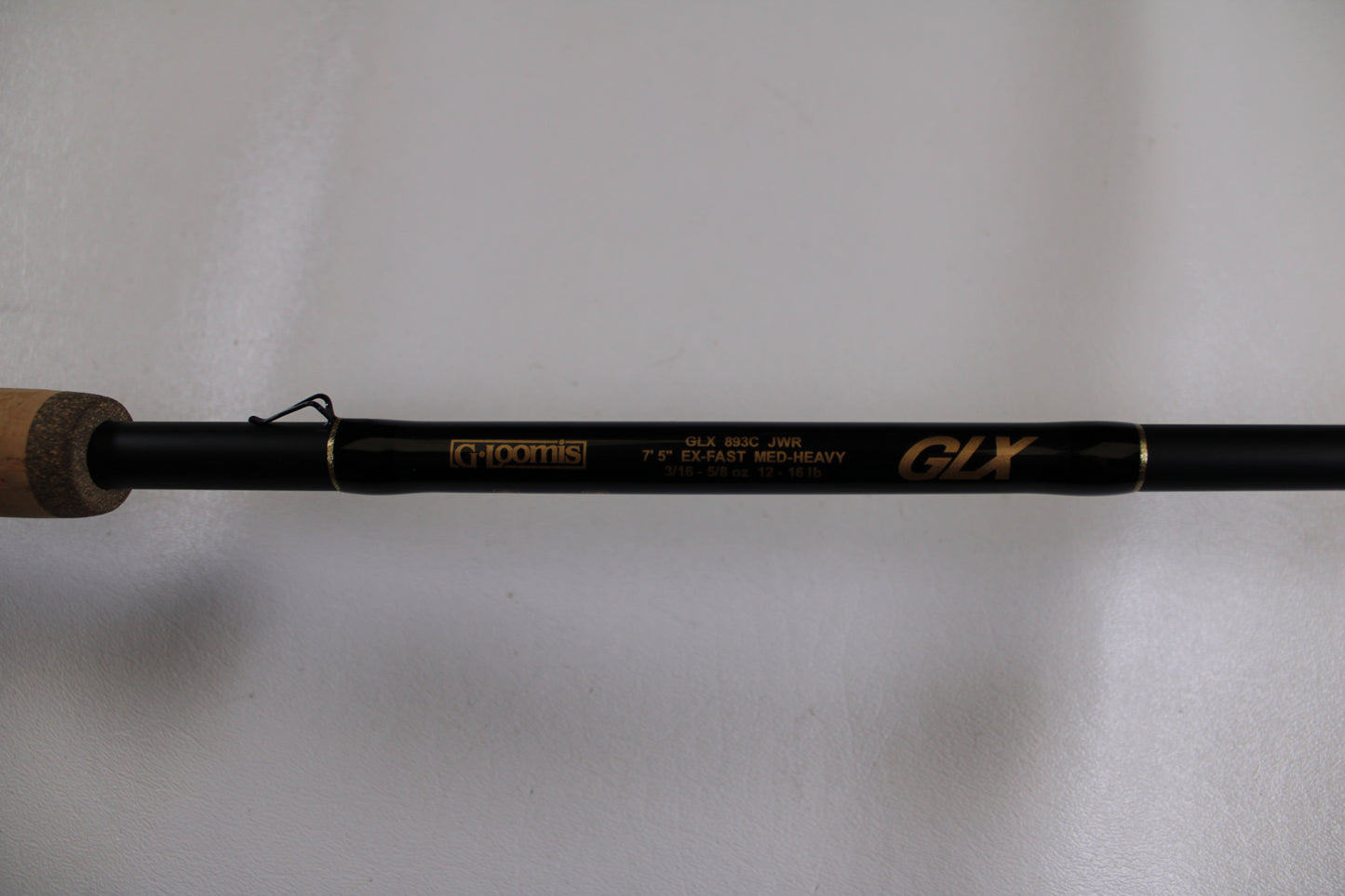 A close-up of a G. Loomis GLX 893c JWR 7'5" Medium Heavy used casting rod in excellent condition, featuring gold text on a black rod and a partially visible cork handle—ideal for Rod and Reel Trade-In or earning store credit.