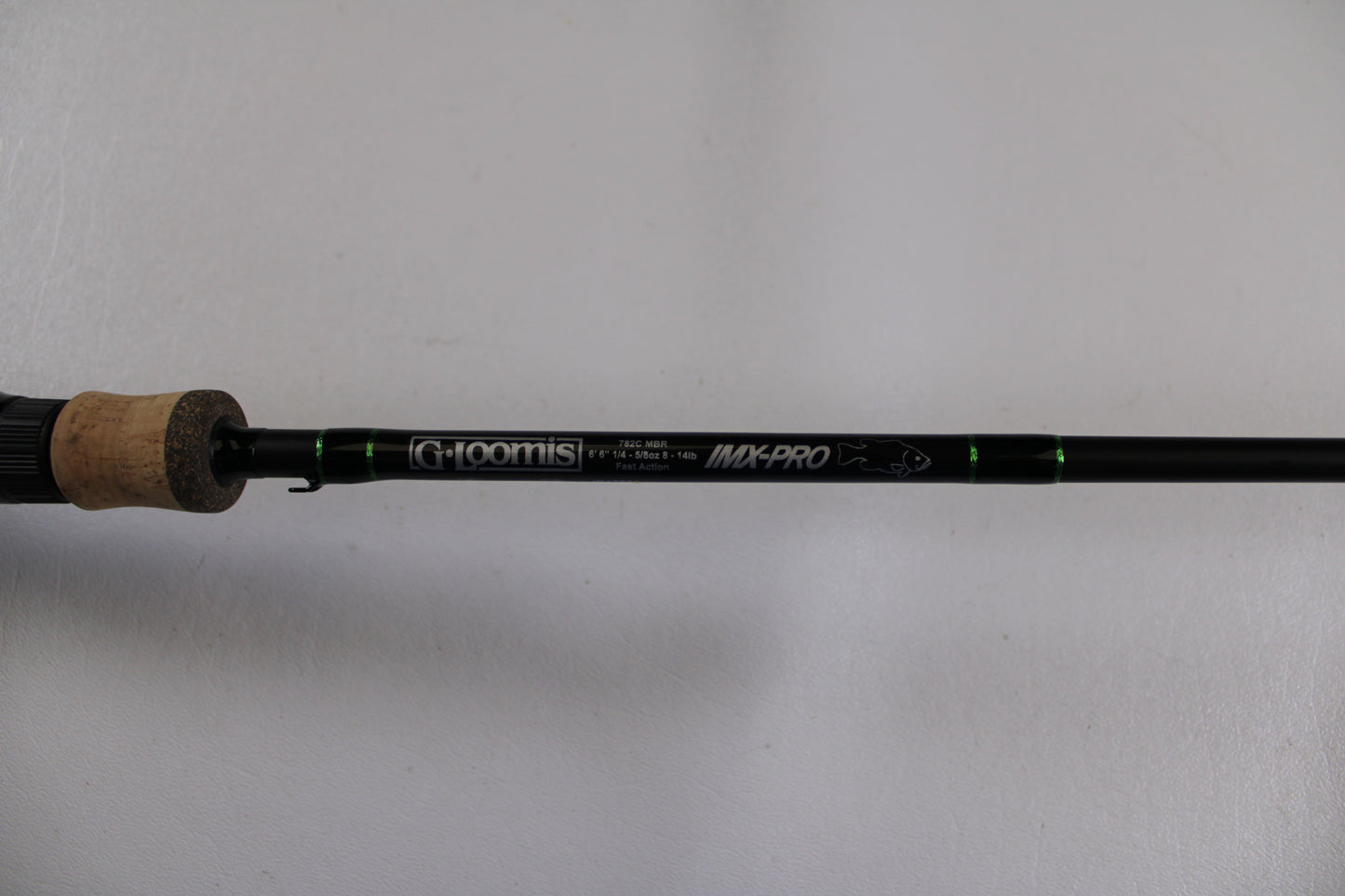 A close-up of the G. Loomis IMX-PRO 782c MBR 6'6" Medium Used Casting Rod in excellent condition shows the brand and model on its black rod with green accents and a cork handle—ideal for Rod and Reel Trade-In or checking used gear.