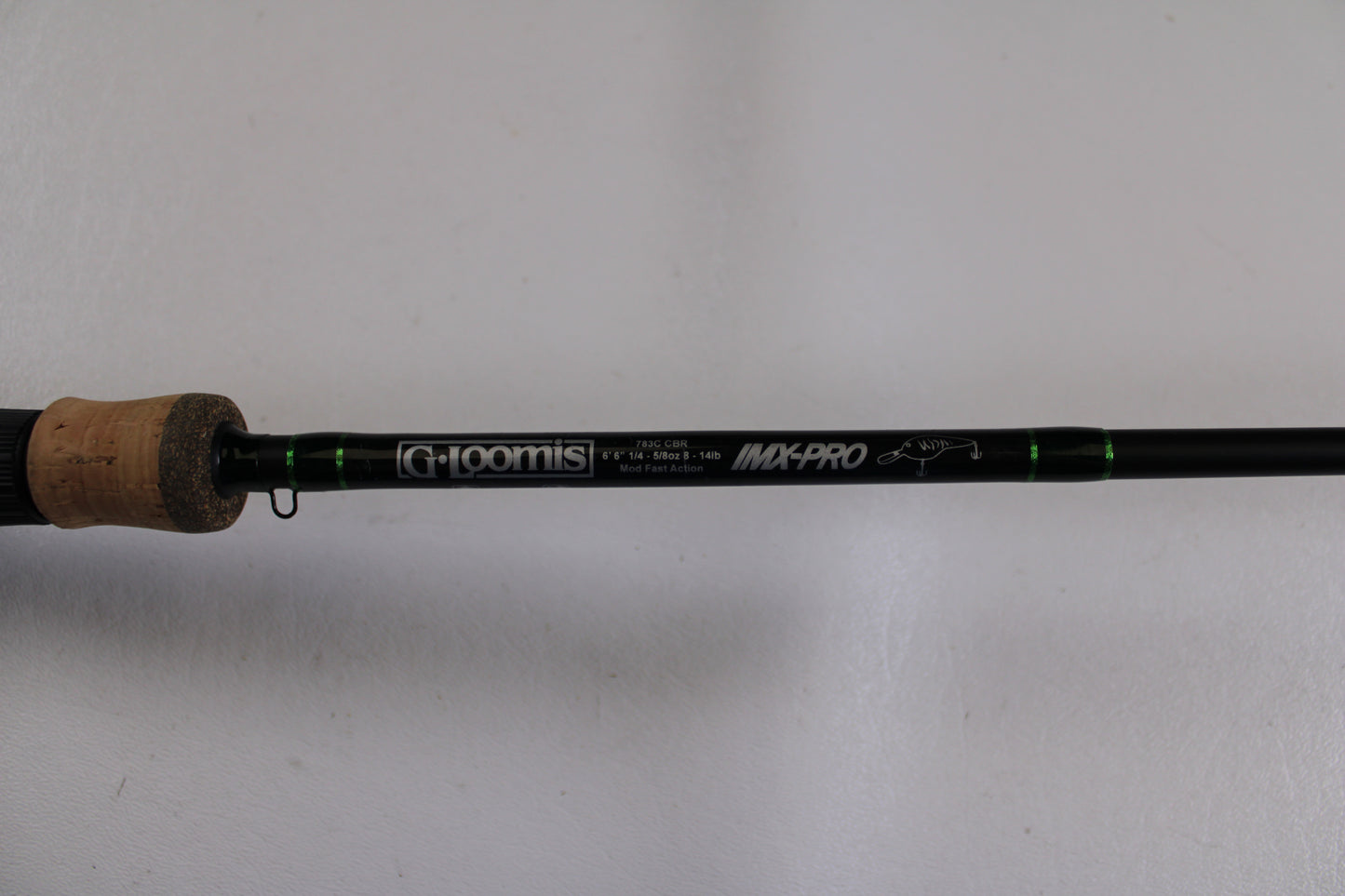 A close-up of a G. Loomis IMX-Pro 783C CBR Used Casting Rod in excellent condition with green accents and a cork handle, shown against a white background—eligible for our Rod and Reel Trade-In Program for store credit.