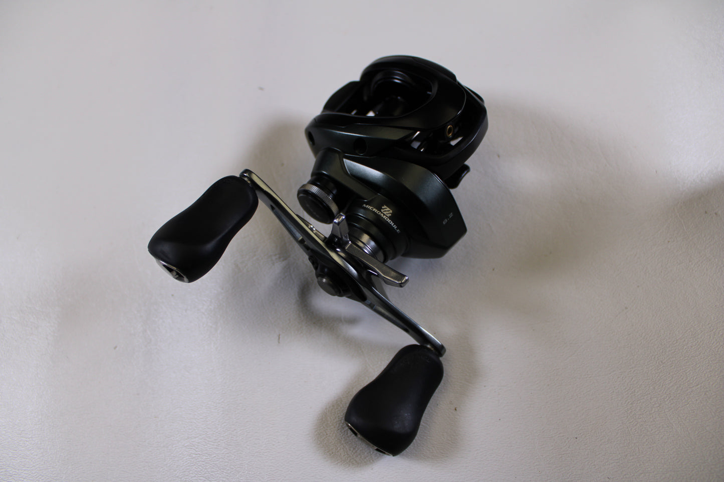 A Shimano Curado CUMGL150 used casting reel in excellent condition with two ergonomic handles is displayed on a plain white surface.