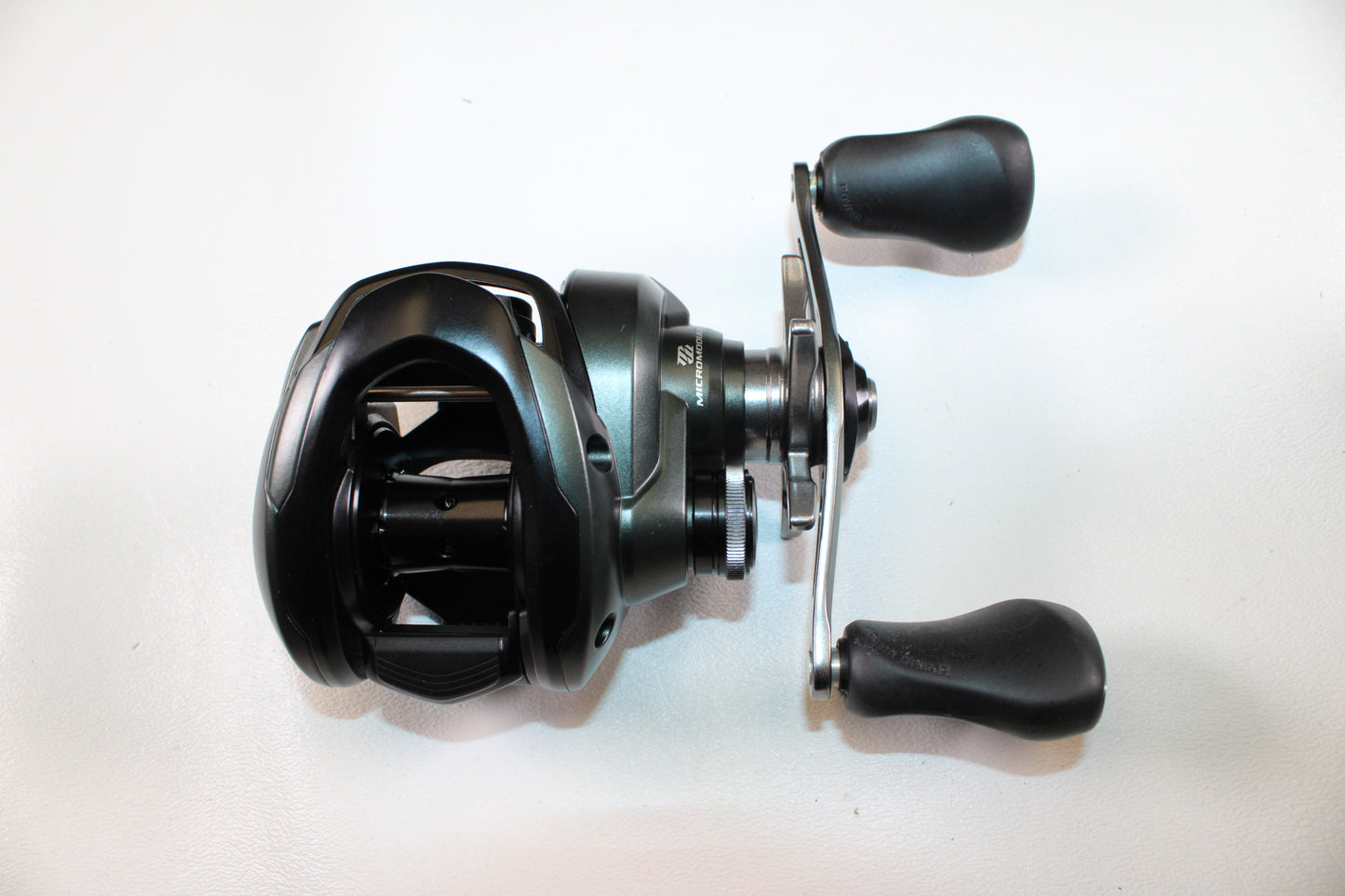 A Shimano Curado CUMGL150 Used Casting Reel by Shimano, in excellent condition with a black and silver finish and two ergonomic handles, displayed on a white surface.