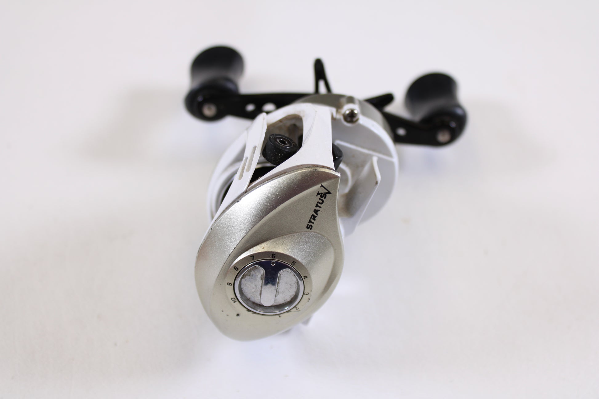 A used Okuma Stratus V 6.4:1 LH casting reel in good condition stands vertically on a white background—perfect for anglers seeking an upgrade through a rod and reel trade-in or exchanging used gear for store credit.