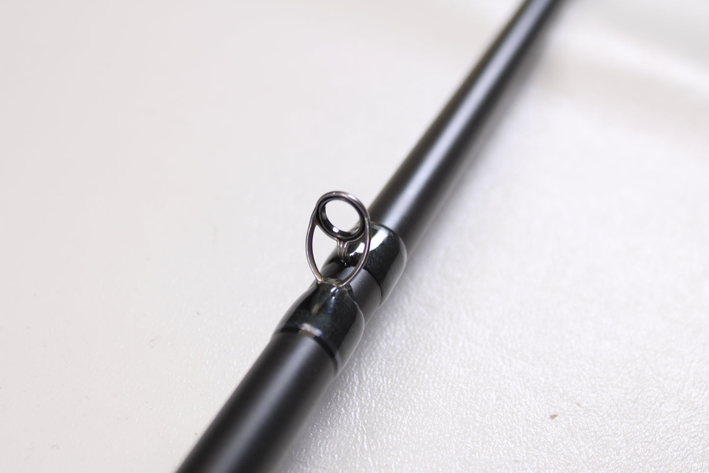 A close-up of the Fenwick World Class Bass WLDB75H-XFC 7'5" Heavy Casting Rod’s black guide ring on a white surface, ideal for bass anglers—available used in excellent condition through our rod and reel trade-in program.