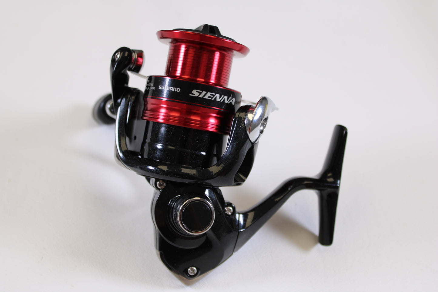A close-up of the Shimano Sienna FG SN2500HGFG used spinning reel in excellent condition features a sleek black body and red spool, displayed on a white background—ideal for those exploring rod and reel trade-in options for store credit.
