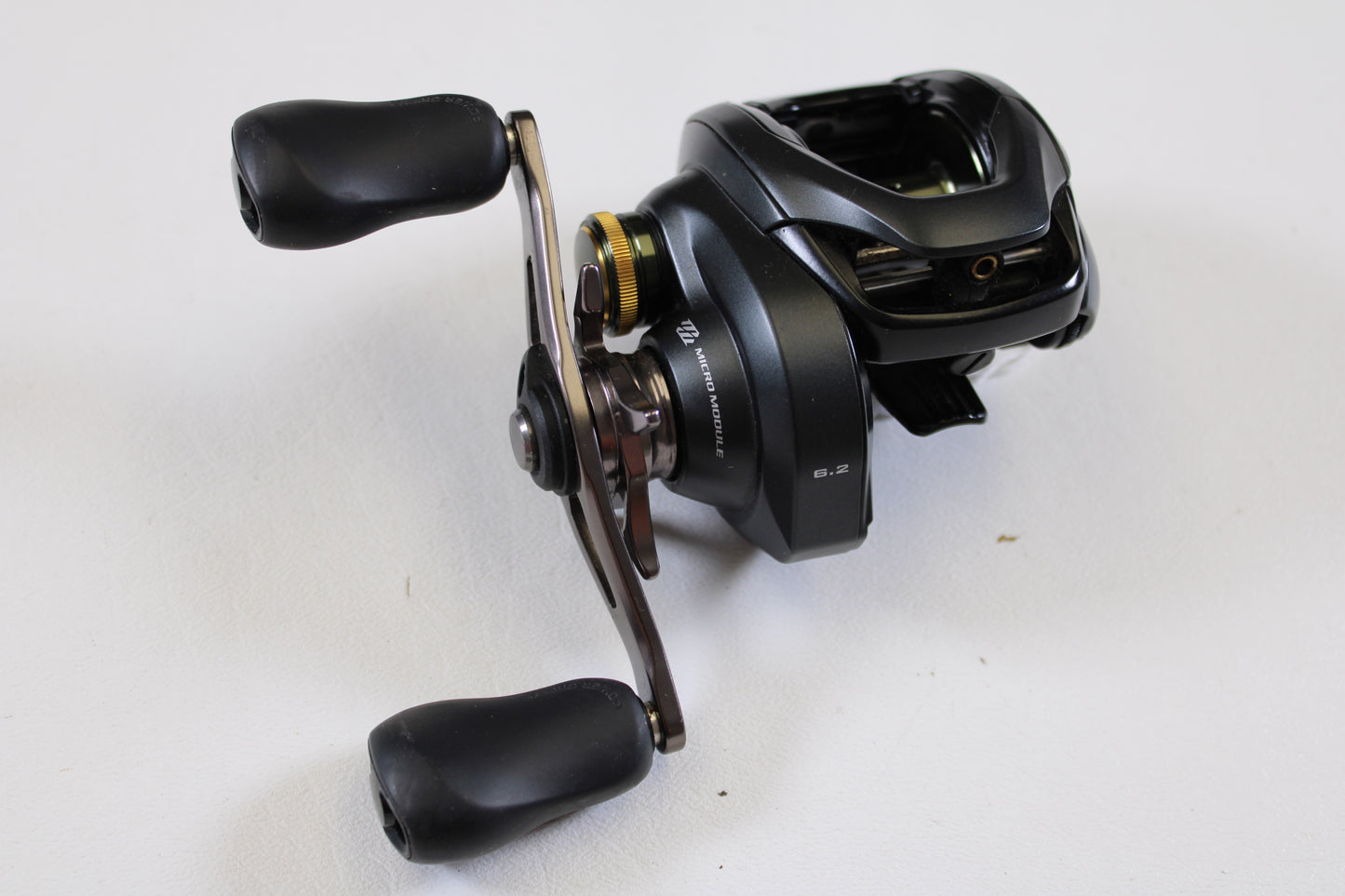 A Shimano Curado 200 K CU200K 6.2:1 RH used casting reel in excellent condition, with black finish, metallic accents, dual rubber handles, and a visible 6.2:1 gear ratio label rests on a white surface. Brand: Shimano.