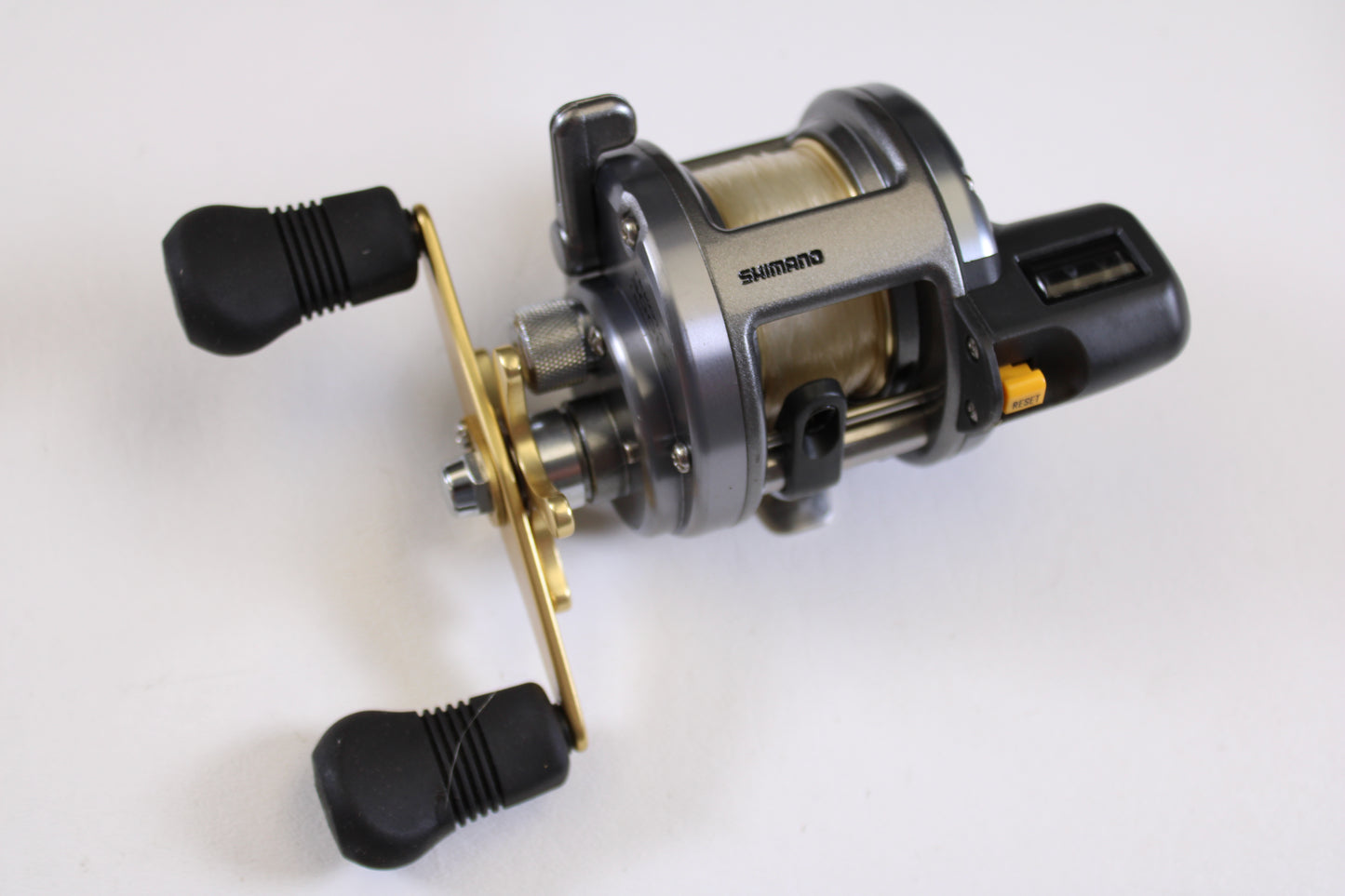 A close-up of a Shimano Tekota Line Counter 300LC casting reel, used but in excellent condition, with black handles, gold crank, and silver body—ideal for anglers trading up through our rod and reel trade-in program for store credit.