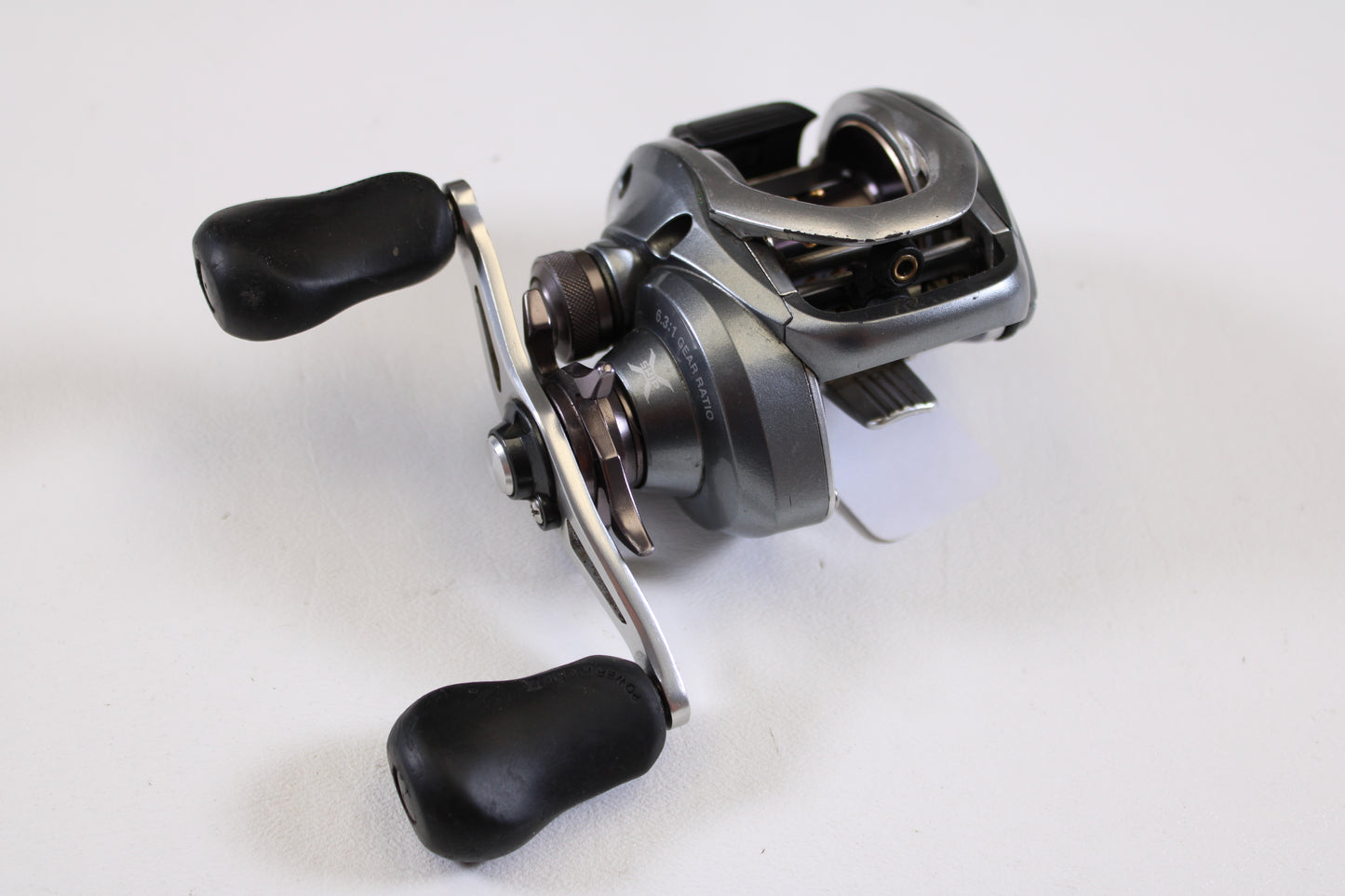 A close-up of a Shimano Curado I CU200I 6.3:1 RH used casting reel in good condition, featuring black handles and shown on a white surface—ideal for anglers seeking reliable, pre-owned Shimano fishing gear.