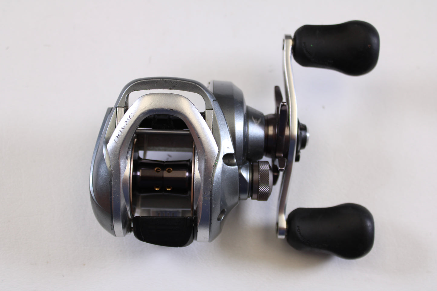 The Shimano Curado I CU200I 6.3:1 RH used casting reel in good condition features a silver and black design with dual black handles—ideal for your fishing gear trade-in or earning store credit.
