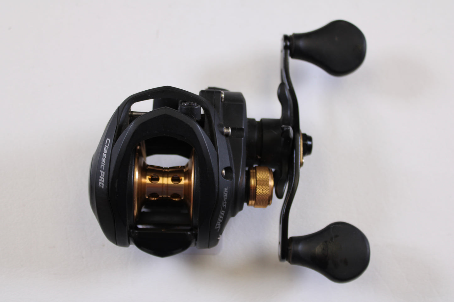 A Lew's Speed Spool Classic Pro CP1SH 7.5:1 RH used baitcasting reel in excellent condition, black and gold with dual rubber handles, is shown from above on a white background—perfect for the rod and reel trade-in program.