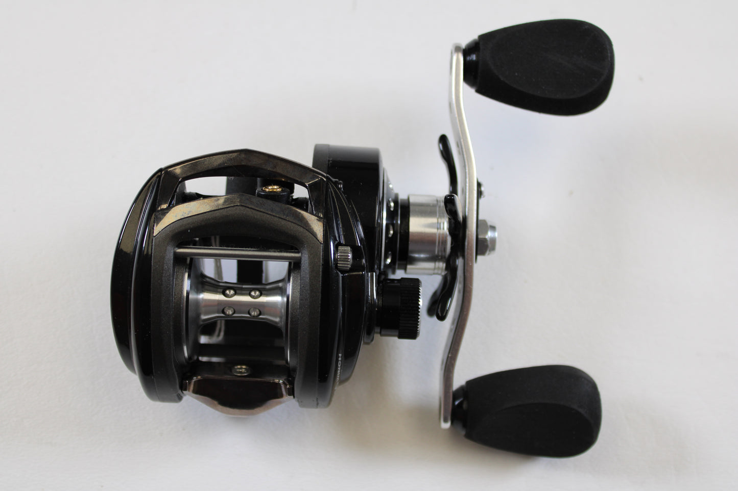 A close-up of an Abu Garcia Revo Winch Gen 3 RVO3 WNCH 5.4:1 RH—Used Casting Reel in Excellent Condition, featuring two handles and a spool on a white surface—ideal for our rod and reel trade-in program for store credit.