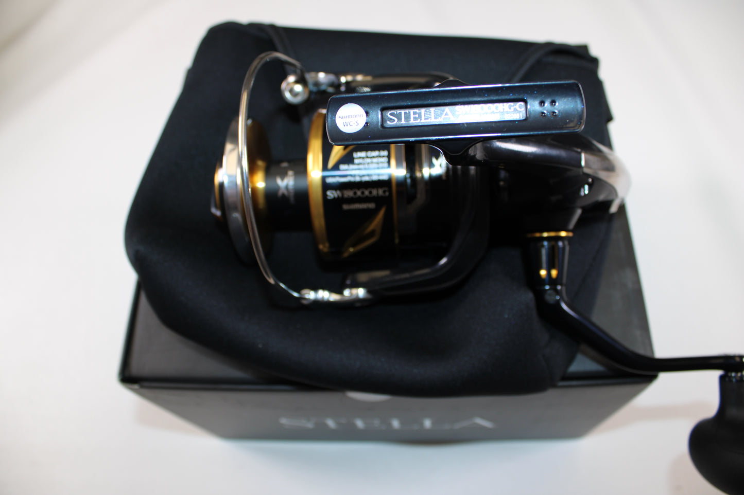 A close-up of a Shimano Stella SW C STLSW18000HGC Used Spinning Reel in mint condition, resting on a soft black pouch atop its box—ideal for those considering our Rod and Reel Trade-In Program for store credit on used Shimano gear.