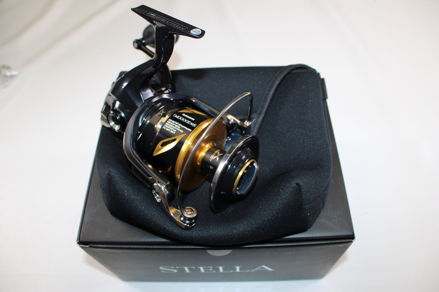 A Shimano Stella SW C STLSW20000PGC Used Spinning Reel in mint condition sits on a black cushion atop a Stella-branded box, ideal for anglers interested in rod and reel trade-in or upgrading used gear for store credit.