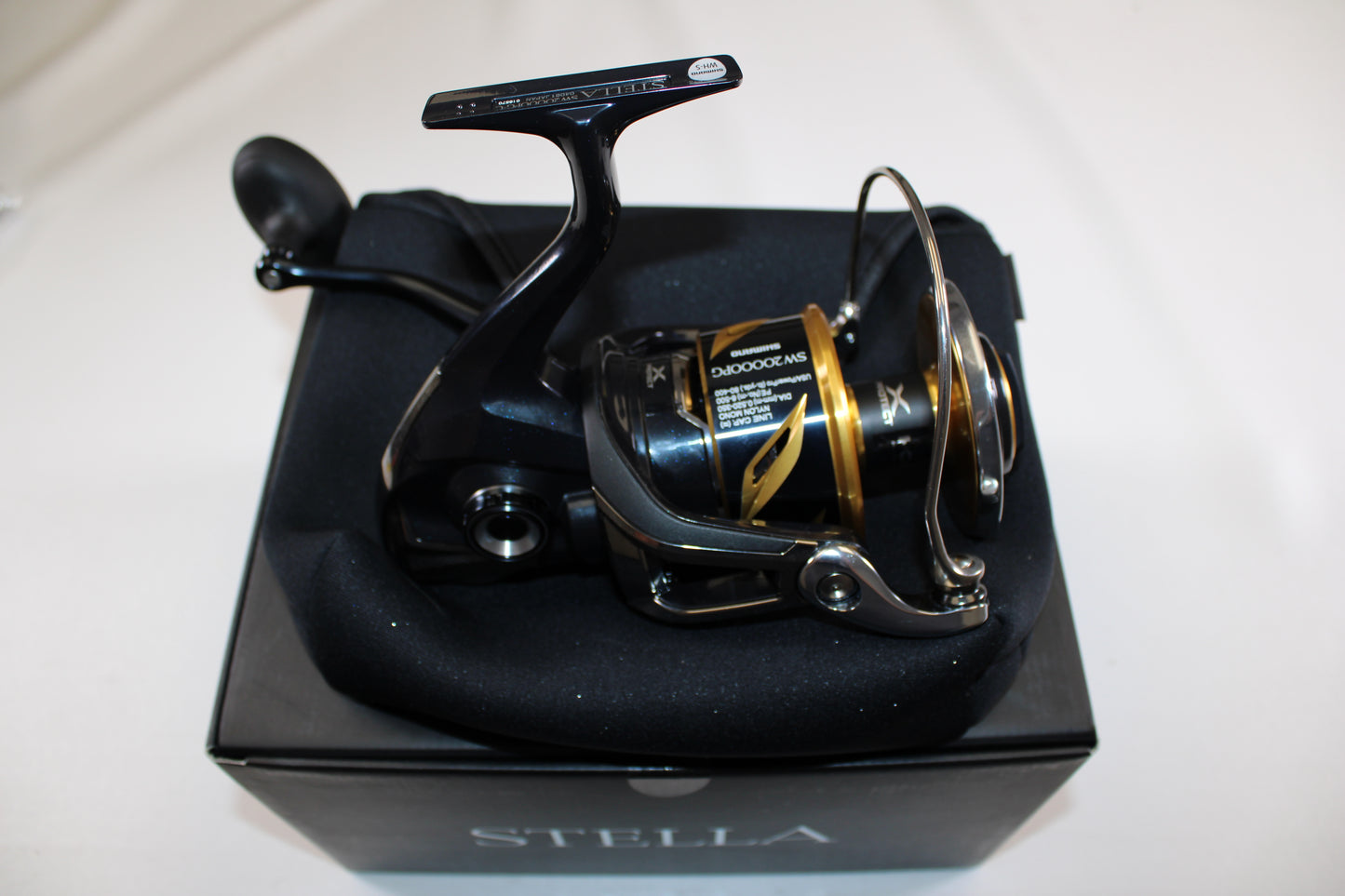 A Shimano Stella SW C STLSW20000PGC Used Spinning Reel in mint condition sits atop a foam pad on a black box, displayed on a white background—ideal for upgrading via our rod and reel trade-in program.